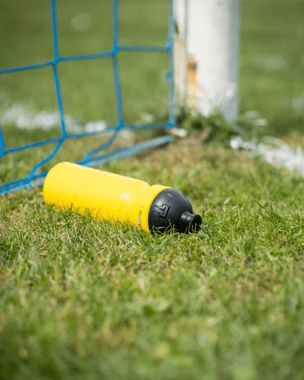 Yellow water bottle in grass near soccer goal for staying healthy