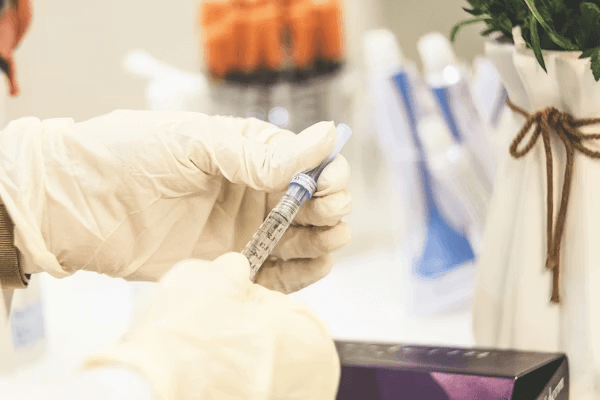 A gloved hand holding a syringe in front of a treatment box