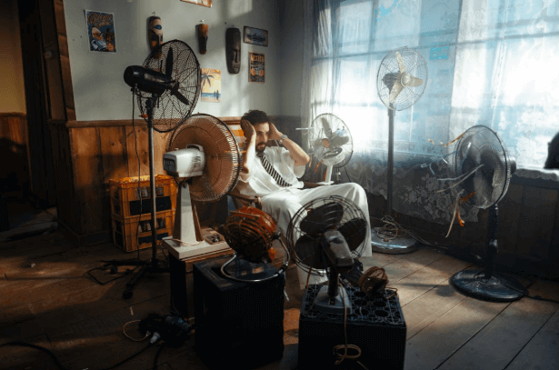 man trying to keep cool with electric fans