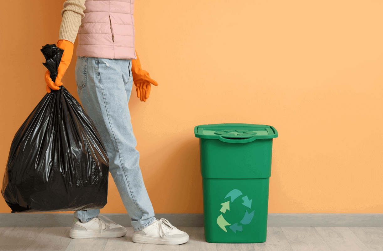 Person standing beside green garbage can