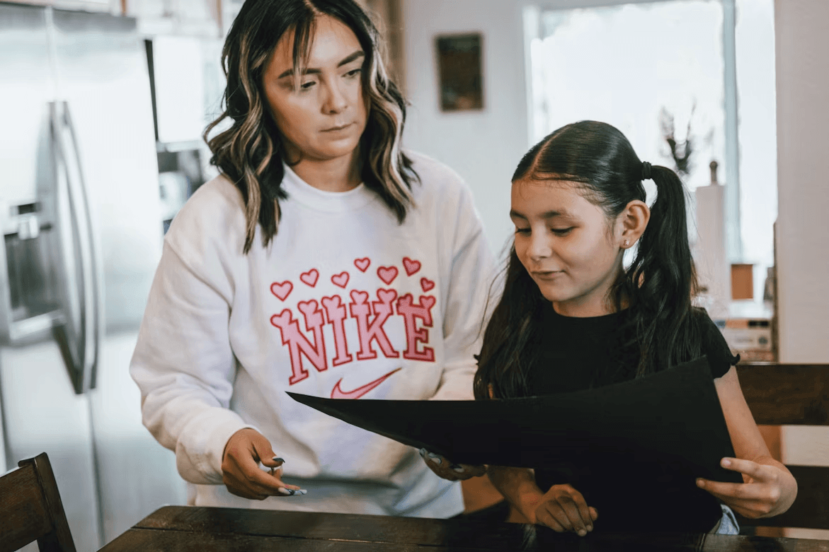 Woman guides little girl at a table, discussing