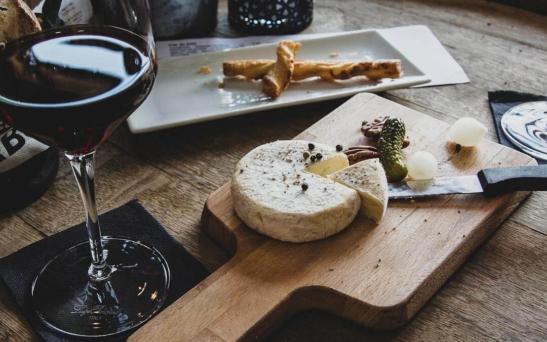 A wooden cutting board with cheese and a glass