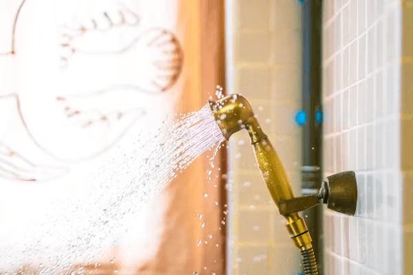 Hand shower spraying water on tiled wall