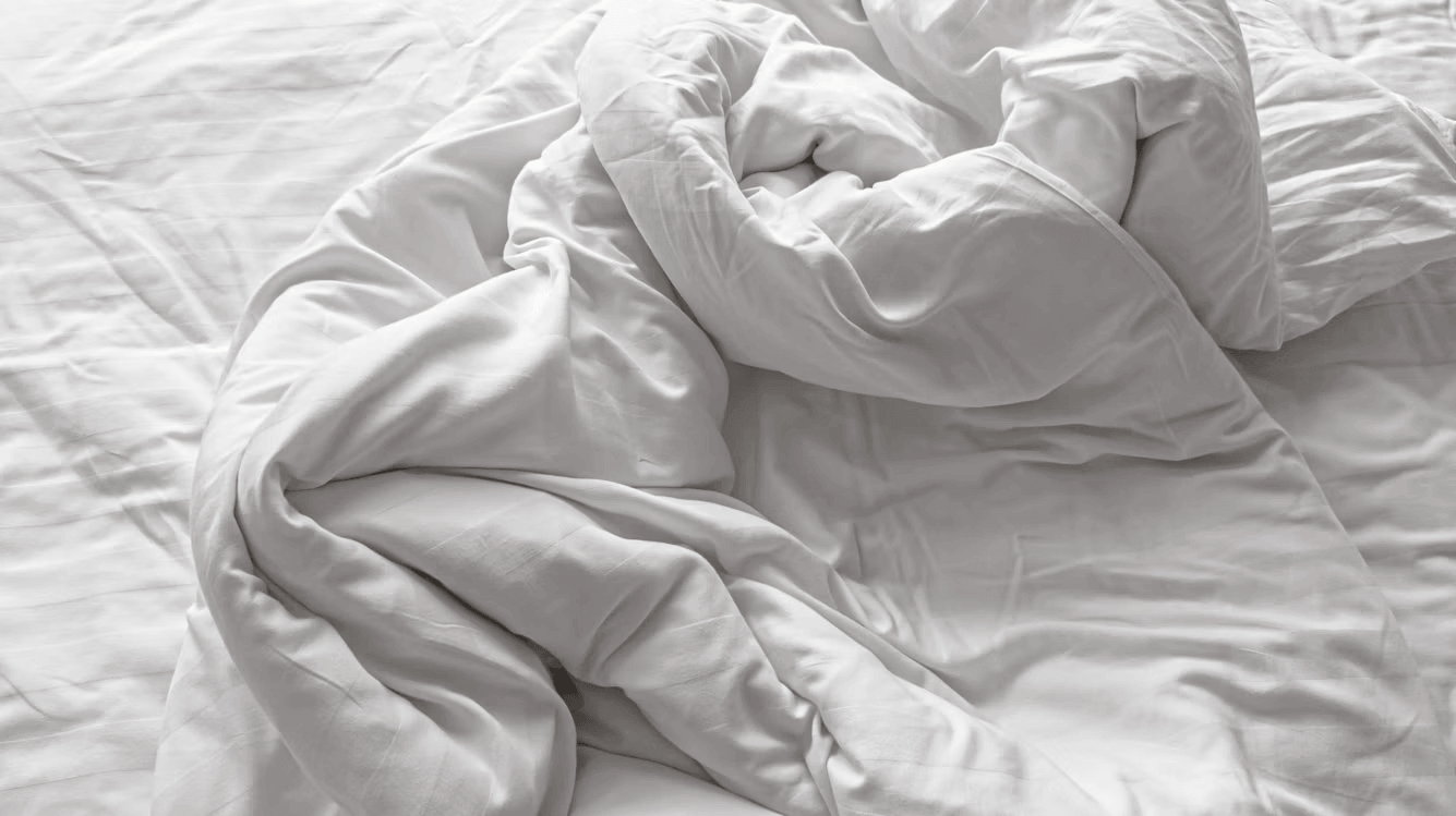 Unmade bed with white sheets and pillows, suggesting
